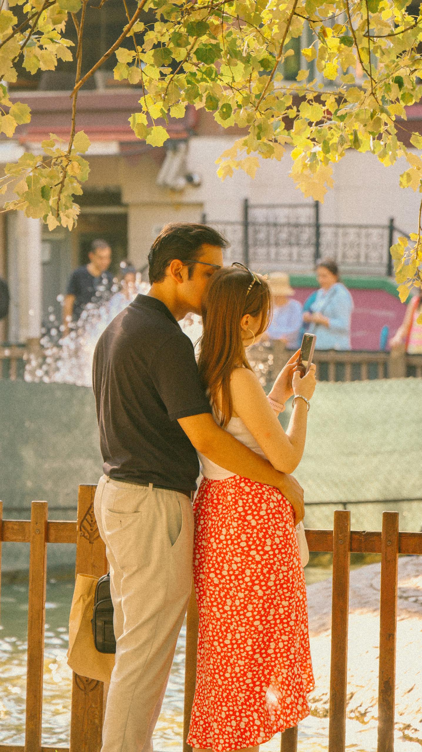 A couple shares a romantic moment, capturing memories in a sunny park.