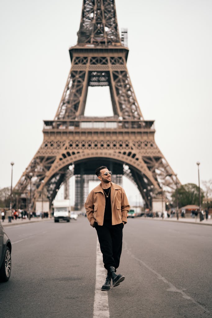 A man walks confidently beneath the iconic Eiffel Tower in Paris, France, creating a classic urban scene.