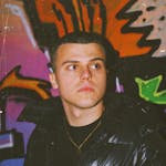 Fashion-forward young man wearing black puffer jacket poses against vibrant graffiti wall.