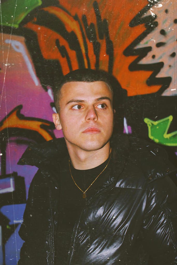 Fashion-forward young man wearing black puffer jacket poses against vibrant graffiti wall.